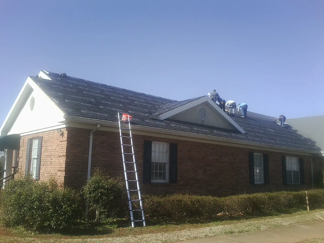 Crew tearing shingles off a brick ranch roof with a ladder set — Emergency Roof Repair work by our crew in Bucyrus